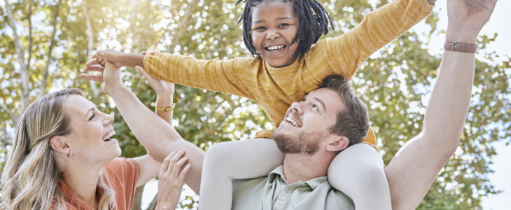 Family, adoption and piggyback in the park with a girl and foster parents having fun together in the park. Diversity, playful and freedom with a mother, father and daughter bonding outdoor in nature